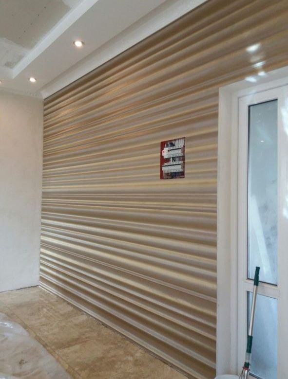 Wnętrze pokoju z dekoracyjną ścianą w poziome prążki, białe listwy sufitowe z oświetleniem punktowym, skrzynka elektryczna na ścianie, widoczny mop przy ościeżnicy.