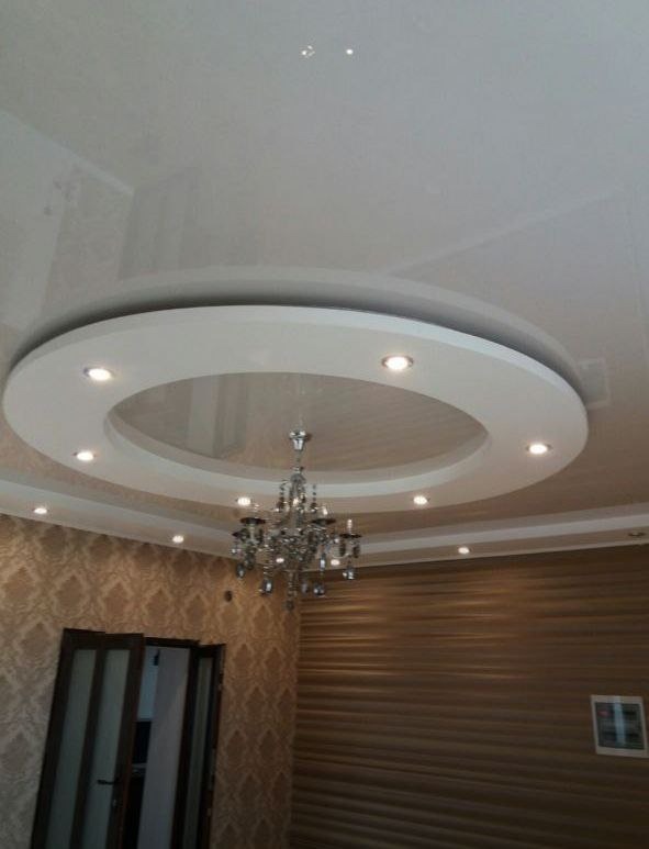 Wykończone wnętrze z podwieszanym sufitem w kształcie okręgu z oświetleniem punktowym i ozdobnym żyrandolem, ściany wykończone tapetą i panelami ściennymi.