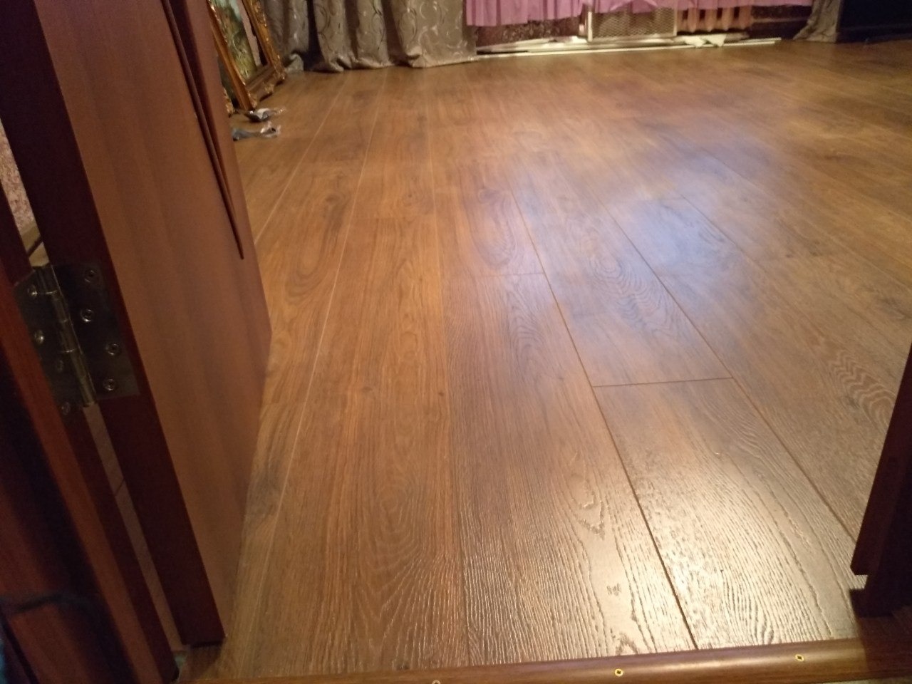 Ułożona podłoga z paneli drewnopodobnych, widoczna z perspektywy wejścia przez drzwi, z widoczną listwą przypodłogową.