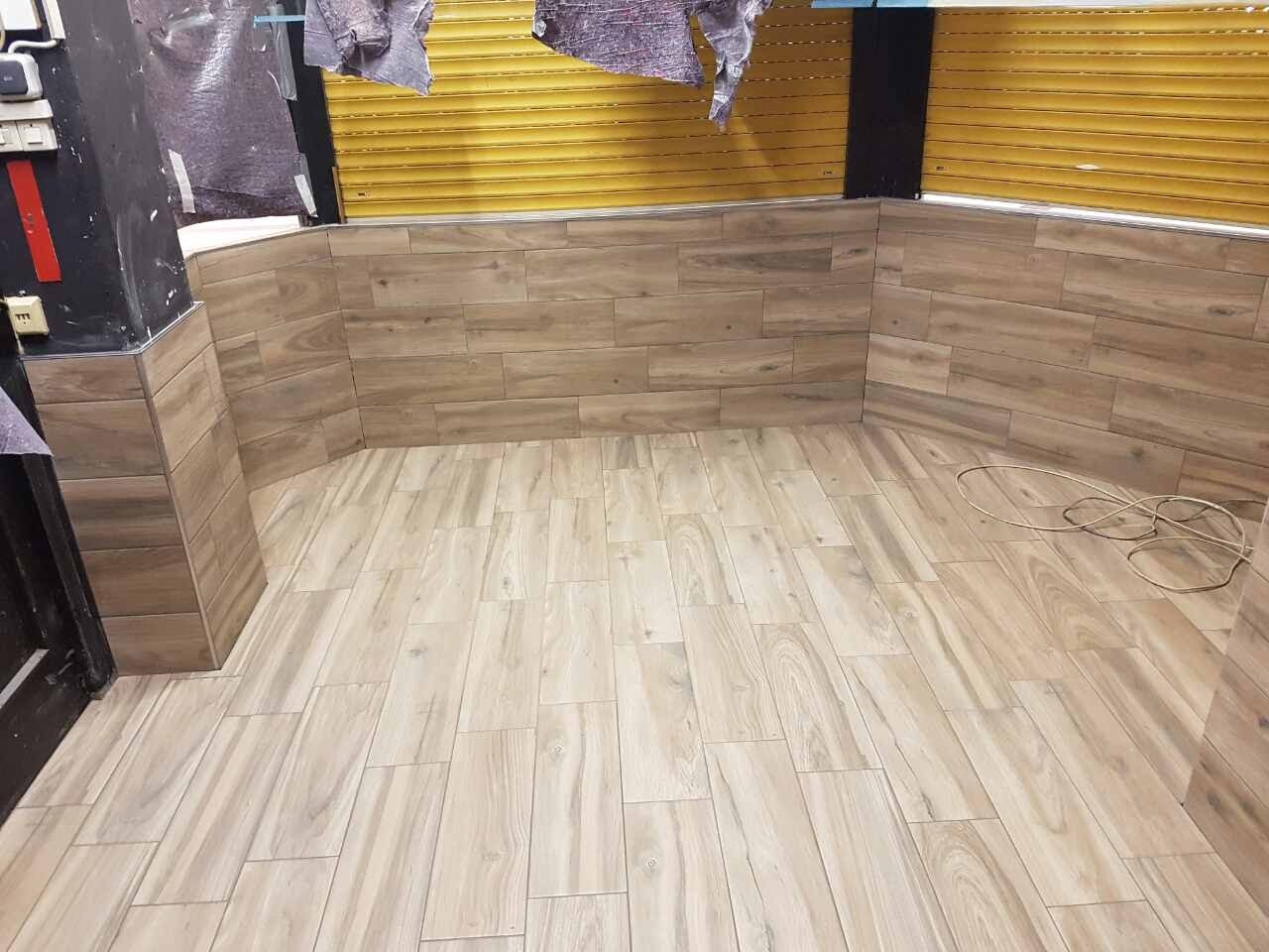 Wykończone wnętrze z podłogą i ścianami wyłożonymi płytkami imitującymi drewno, widoczne zwisające kable i fragment zwiniętej rolety okiennej.