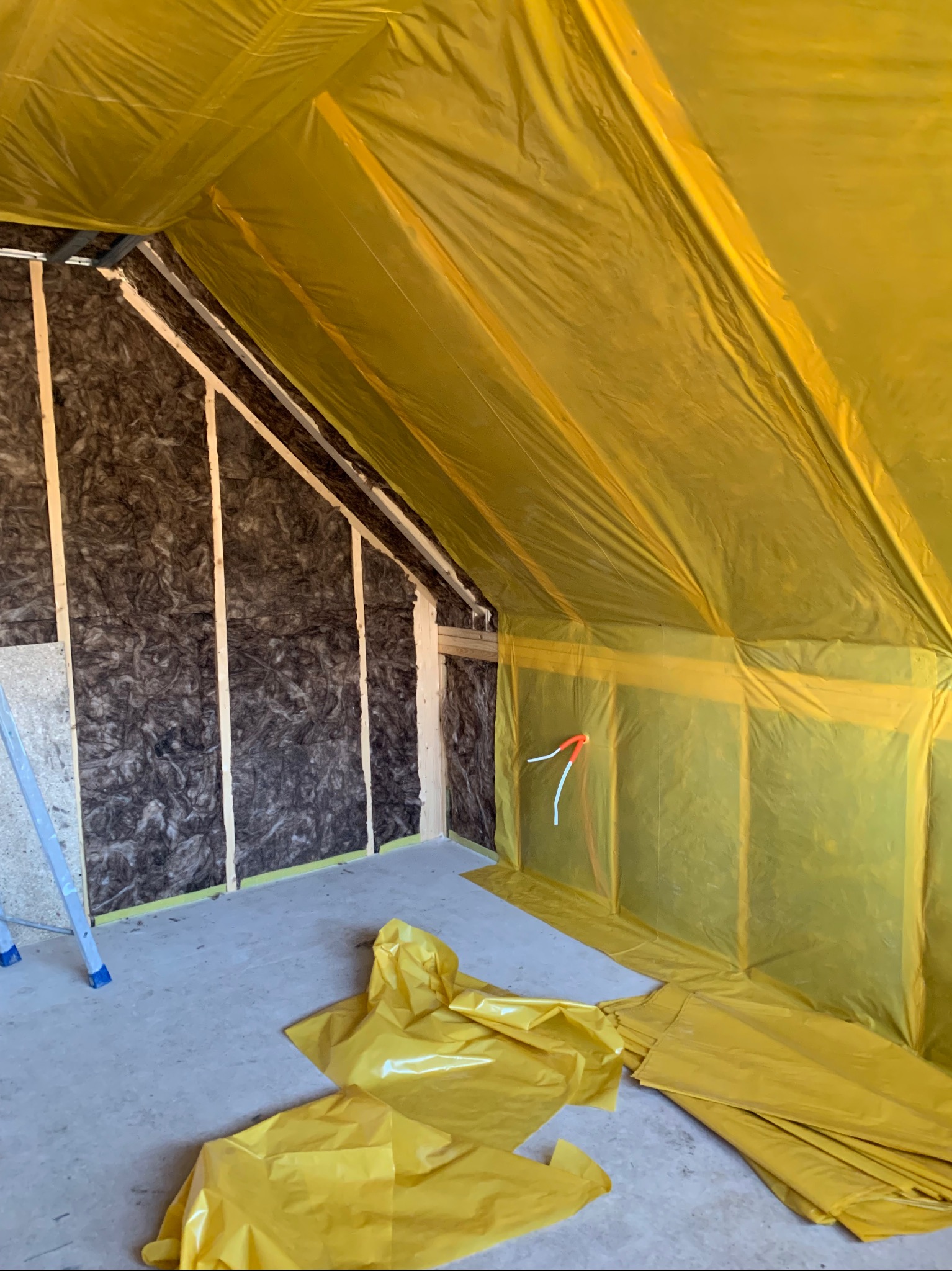 Izolacja poddasza wełną mineralną i folią paroizolacyjną w Żywcu. Widoczne drewniane elementy konstrukcyjne i fragment drabiny.