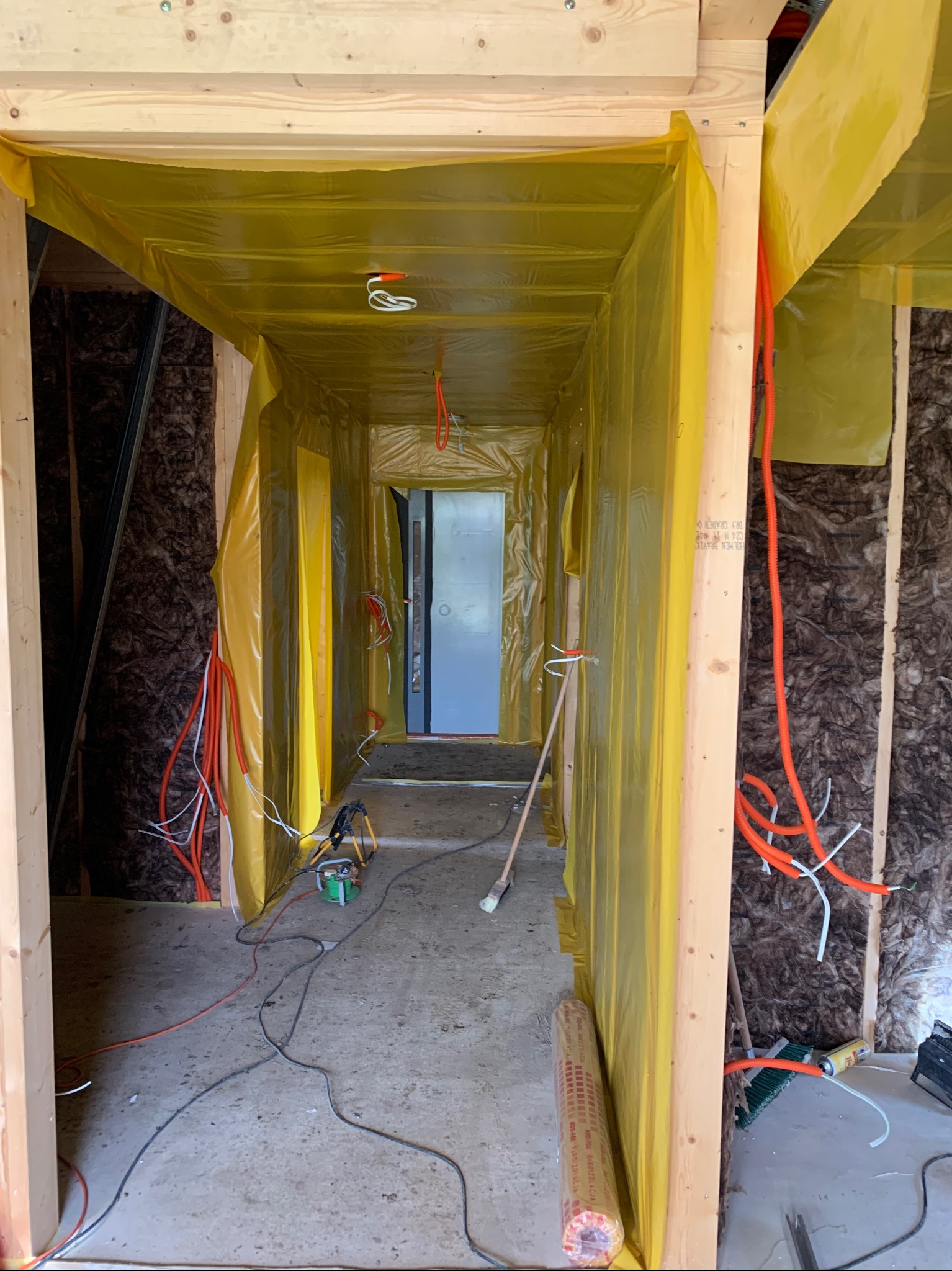 Wnętrze w trakcie prac wykończeniowych: izolacja ścian wełną mineralną, folia paroizolacyjna, instalacja elektryczna w peszlach. Widoczne narzędzia i materiały budowlane.