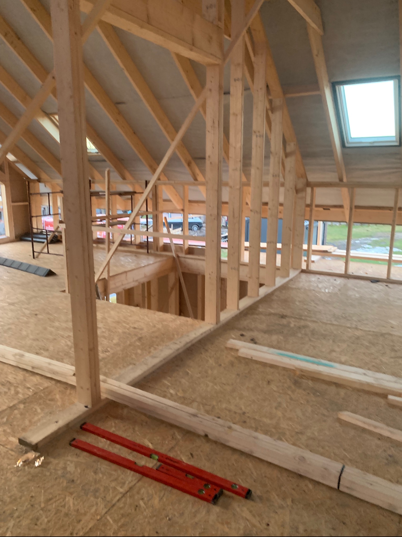 Surowa konstrukcja drewniana poddasza z oknem dachowym, widoczne poziomice i płyty OSB. Etap budowy domu jednorodzinnego, wnętrze w stanie deweloperskim.