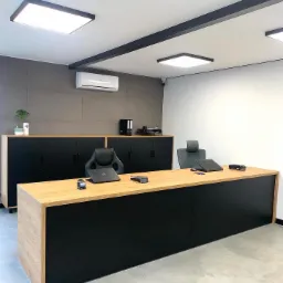 Nowoczesne biuro z dużym biurkiem z blatem drewnianym i czarnym frontem, czarne szafki i szara ściana w tle, minimalistyczny wystrój.