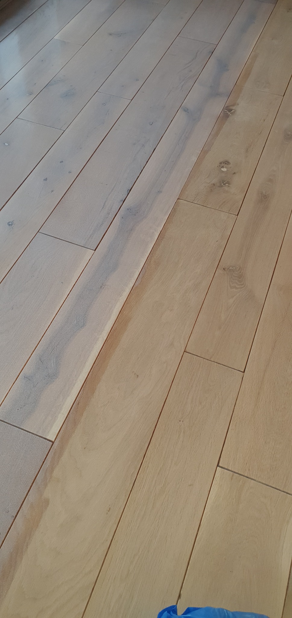 Jasne, drewniane deski parkietu ułożone ukośnie, z widocznymi naturalnymi przebarwieniami i słojami drewna, fragment niebieskiej tkaniny w rogu.