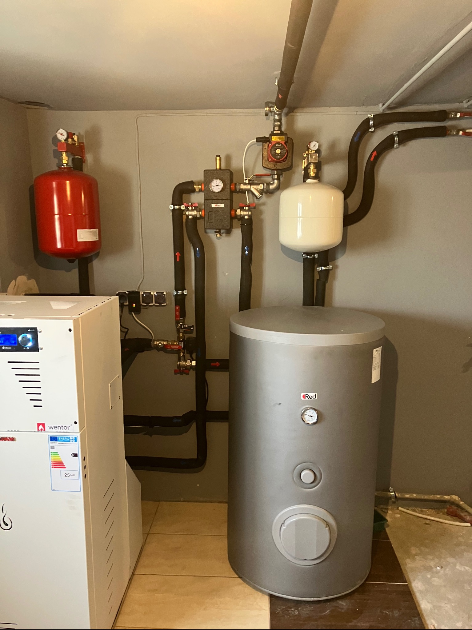 Złożona instalacja grzewcza z kotłem Wentor, zbiornikiem Red i licznymi rurami, zaworami oraz manometrami. Widoczne elementy instalacji centralnego ogrzewania.