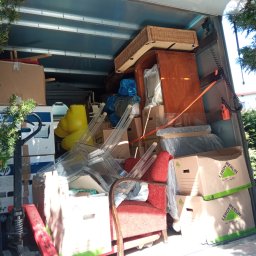 AR-TRANS Agata Rudnicka - Wnętrze załadowanego busa przeprowadzkowego z meblami (czerwony fotel, przezroczyste krzesła), kartonami (w tym Leroy Merlin) i sprzętem, widok z zewnątrz przez otwarte drzwi, częściowo zasłonięte...
