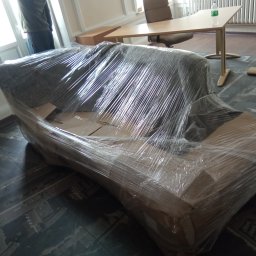 AR-TRANS Agata Rudnicka - Sofa owinięta folią stretch, przygotowana do transportu w pomieszczeniu z biurkiem i krzesłem w tle.