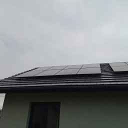 SkyVolt Rafał Kornas - Panele słoneczne zamontowane na dachu domu pokrytego ciemną dachówką, widok z dołu na tle pochmurnego nieba.