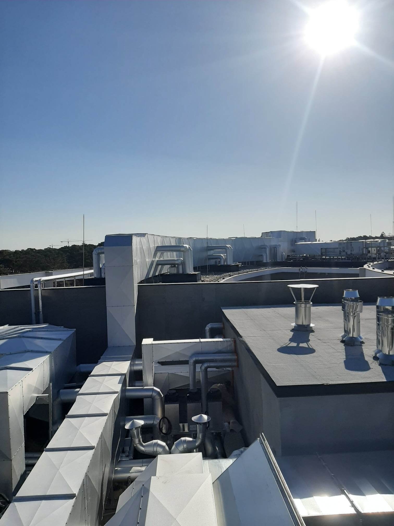 System kanałów wentylacyjnych na dachu budynku, widok z góry, w tle błękitne niebo i ostre słońce.