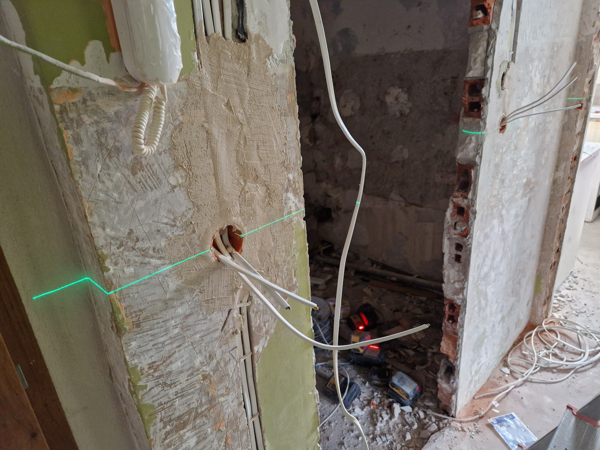 Wnętrze w trakcie remontu: przewody elektryczne wystające ze ściany, wyznaczona laserowo linia pozioma, widoczne narzędzia i gruz.