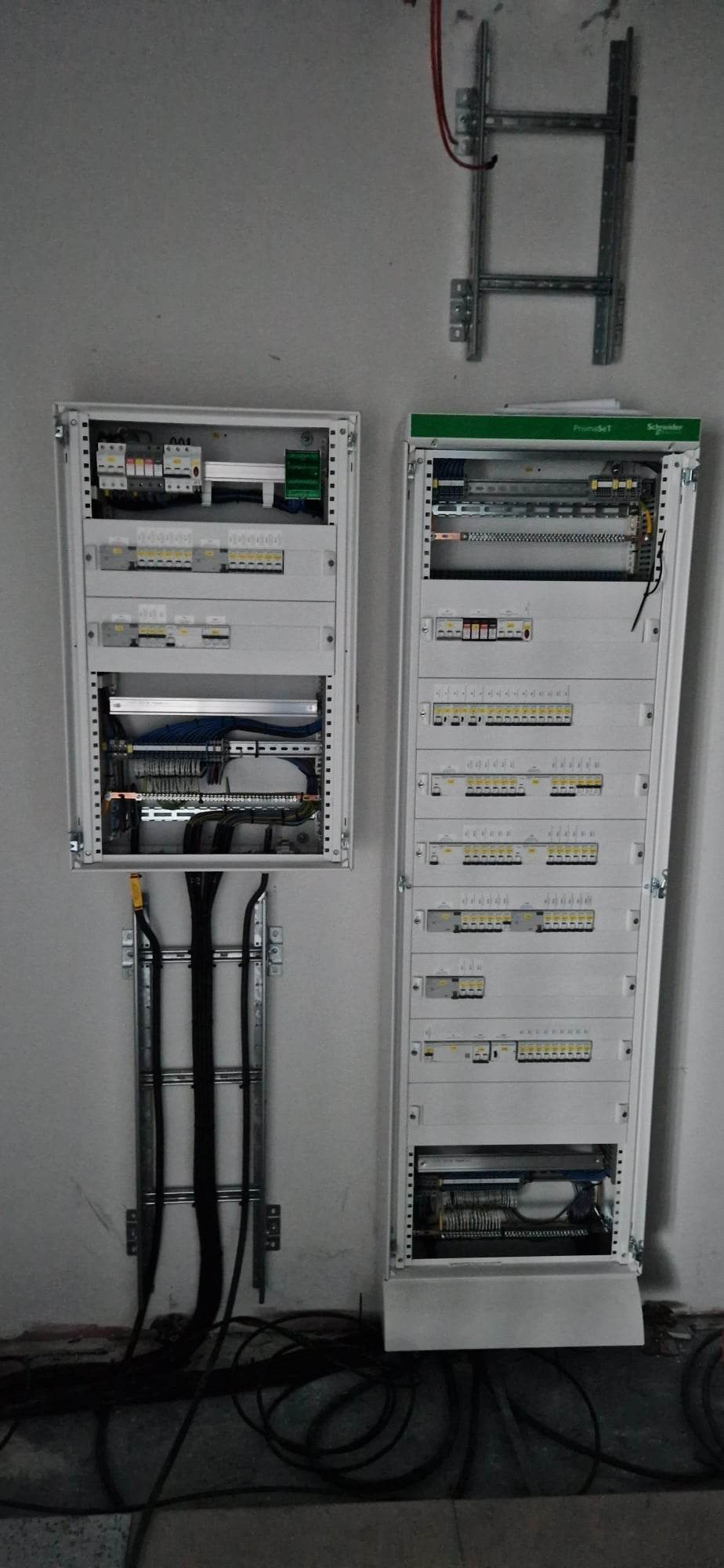 Dwa rozdzielnice elektryczne zamontowane na ścianie, widoczne kable i elementy instalacji wewnątrz szaf.