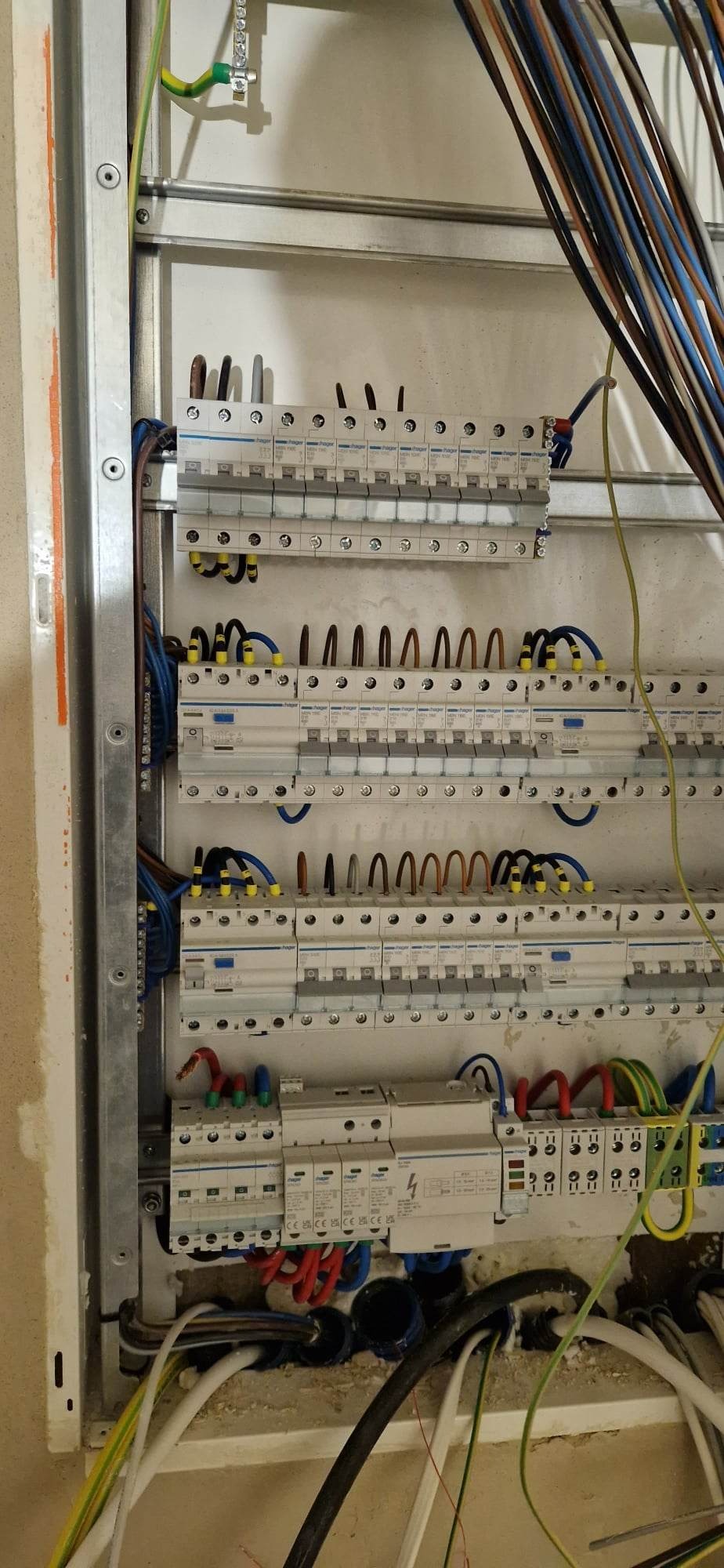 Rozdzielnica elektryczna w trakcie montażu, widoczne zabezpieczenia nadprądowe, różnicowoprądowe oraz przewody w różnych kolorach podłączone do listew zaciskowych wewnątrz metalowej obudowy.