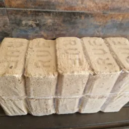 Zapakowany w folię pakiet brykietu drzewnego RUF leżący na metalowej kratce, z widoczną fakturą i napisem na każdym z brykietów.