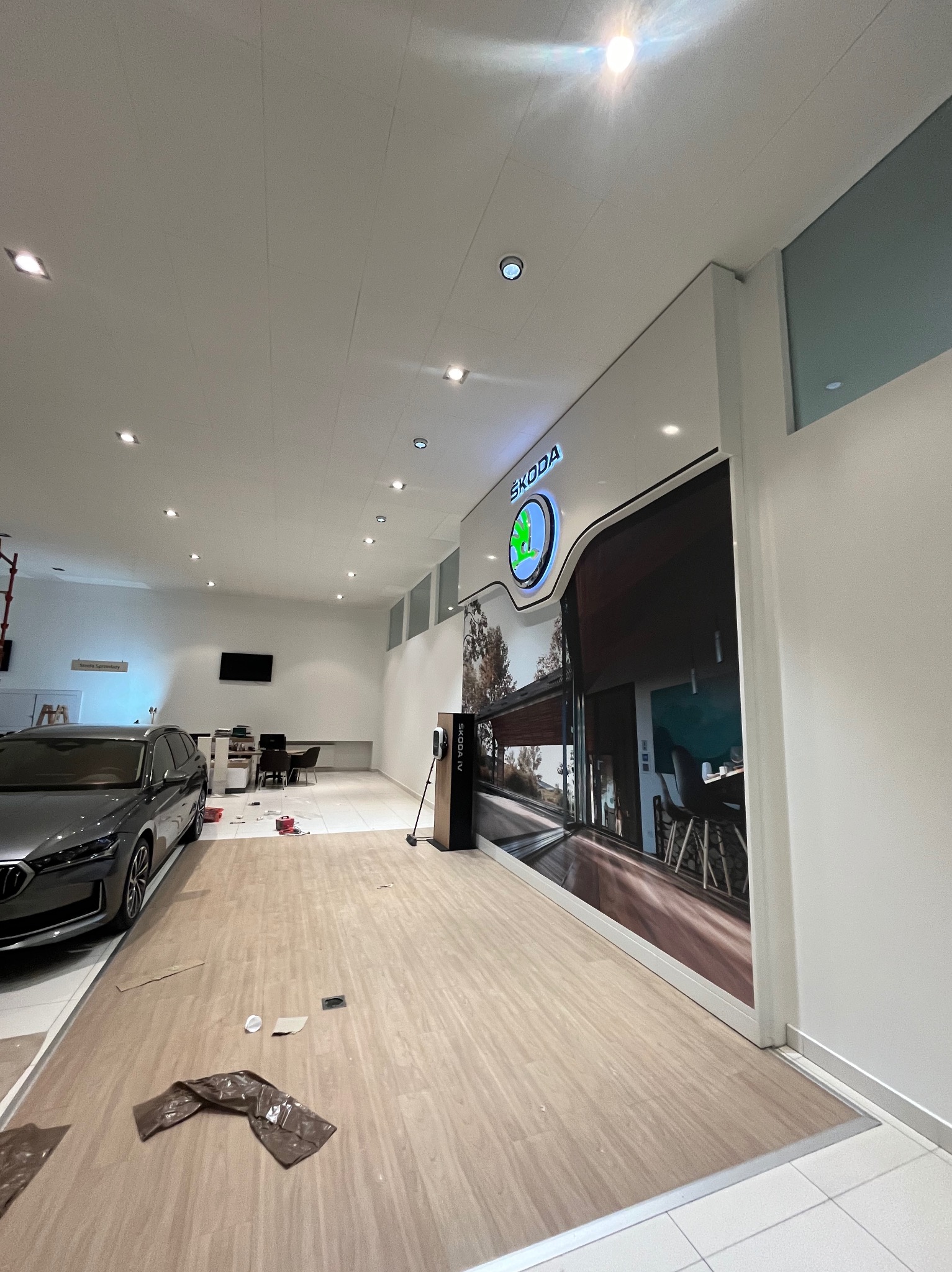Wnętrze salonu samochodowego marki Skoda w trakcie prac wykończeniowych: widoczny samochód, logo marki na ścianie, elementy podłogi zabezpieczone folią i kartonem, przygotowane do położenia nowej...