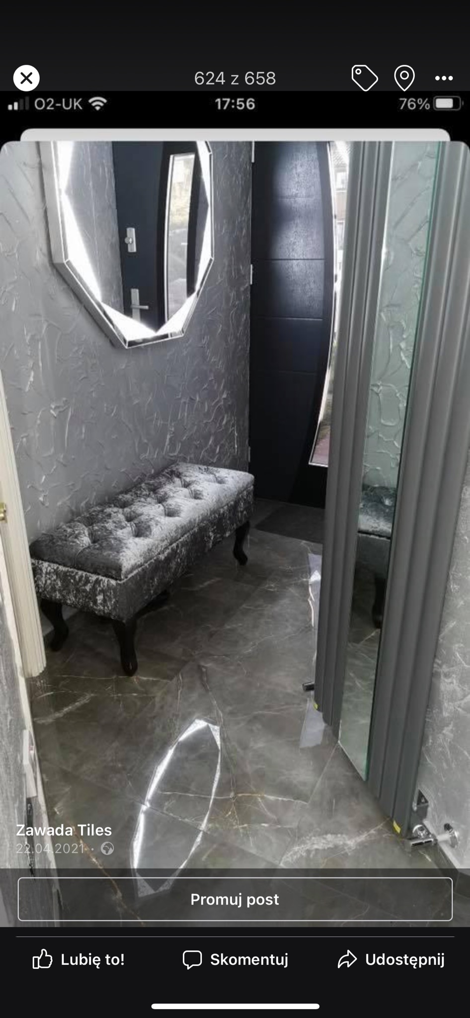 Szare wnętrze przedpokoju z marmurową podłogą, tapetą o fakturze betonu, lustrem w kształcie ośmiokąta i welurową ławką na toczonych nogach, widok na czarne drzwi wejściowe.