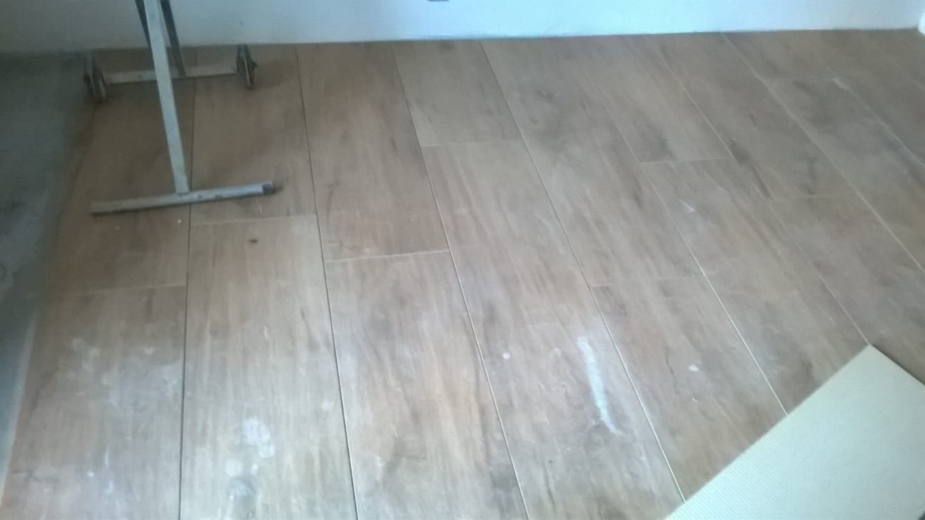 Ułożona podłoga z płytek imitujących drewno w trakcie prac wykończeniowych, widoczne narzędzia i resztki zaprawy.