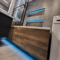 Gold Time Mykola Naboka - Nowoczesna łazienka z podświetlaną wanną obłożoną drewnopodobnymi panelami, kabina prysznicowa z czarnymi profilami, szare płytki ścienne z niszami podświetlonymi niebieskim światłem LED, pralka...