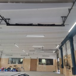 Gold Time Mykola Naboka - Wnętrze warsztatu z oświetleniem LED, widoczne podnośniki samochodowe, instalacje elektryczne na suficie i okna z widokiem na zewnątrz.