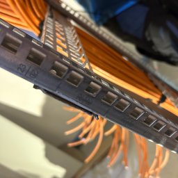 Gold Time Mykola Naboka - Pomarańczowe przewody elektryczne ułożone w metalowej perforowanej korycie kablowej, widok z bliska na oznaczenia na korycie.