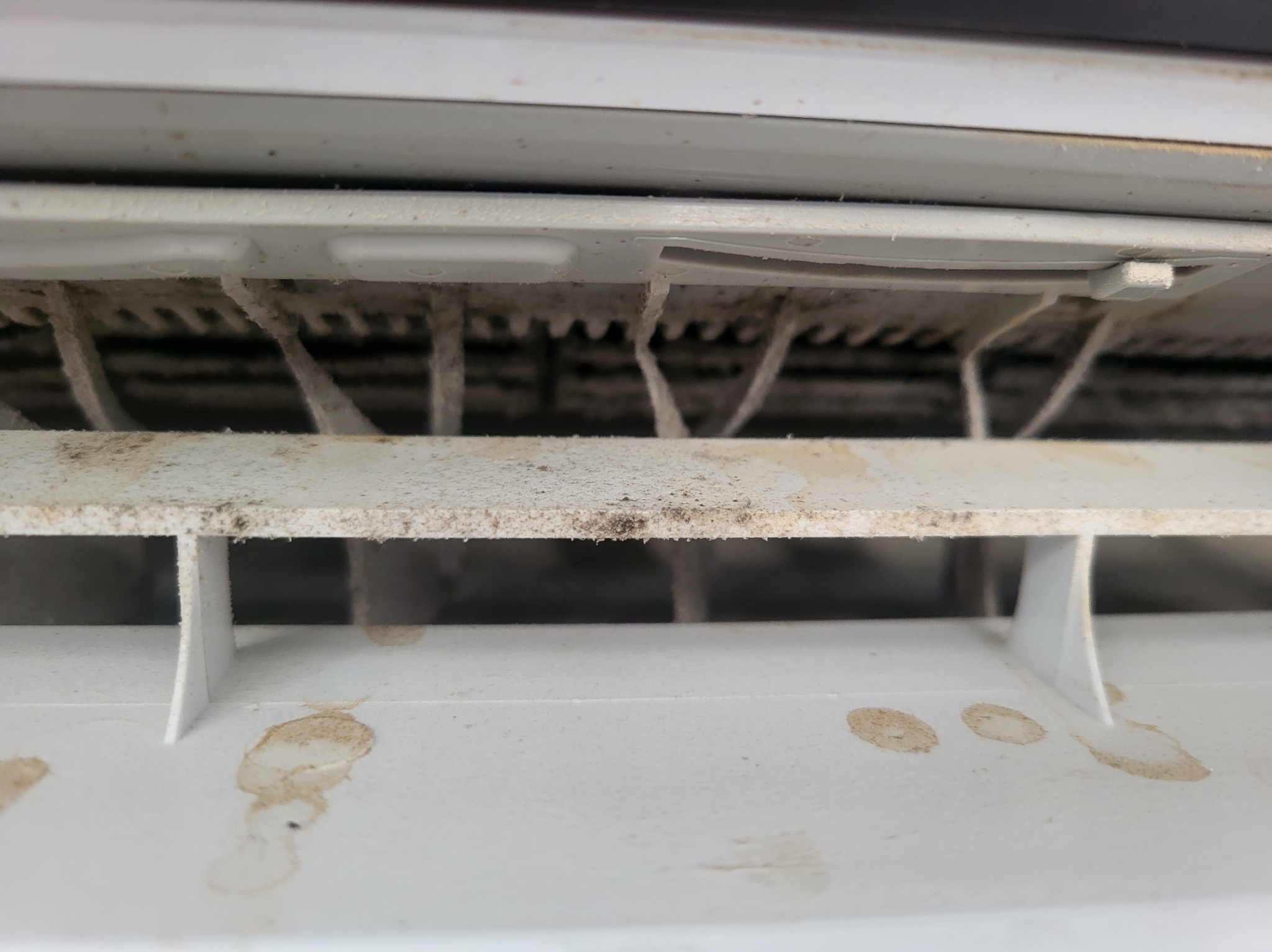 Zabrudzone, białe żaluzje klimatyzatora z widocznymi plamami i kurzem, wymagające czyszczenia.