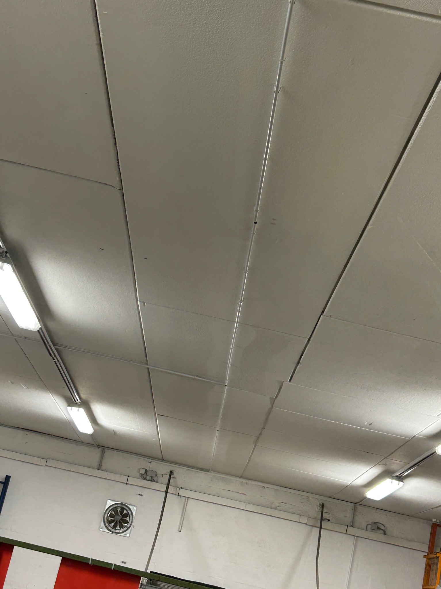 Sufit podwieszany z widocznymi panelami, oświetleniem LED i kratką wentylacyjną na ścianie, sfotografowany pod kątem.