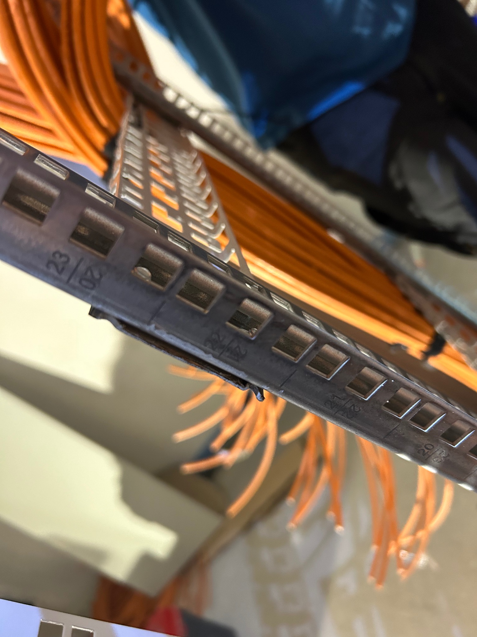 Pomarańczowe przewody elektryczne ułożone w metalowej perforowanej korycie kablowej, widok z bliska na oznaczenia na korycie.