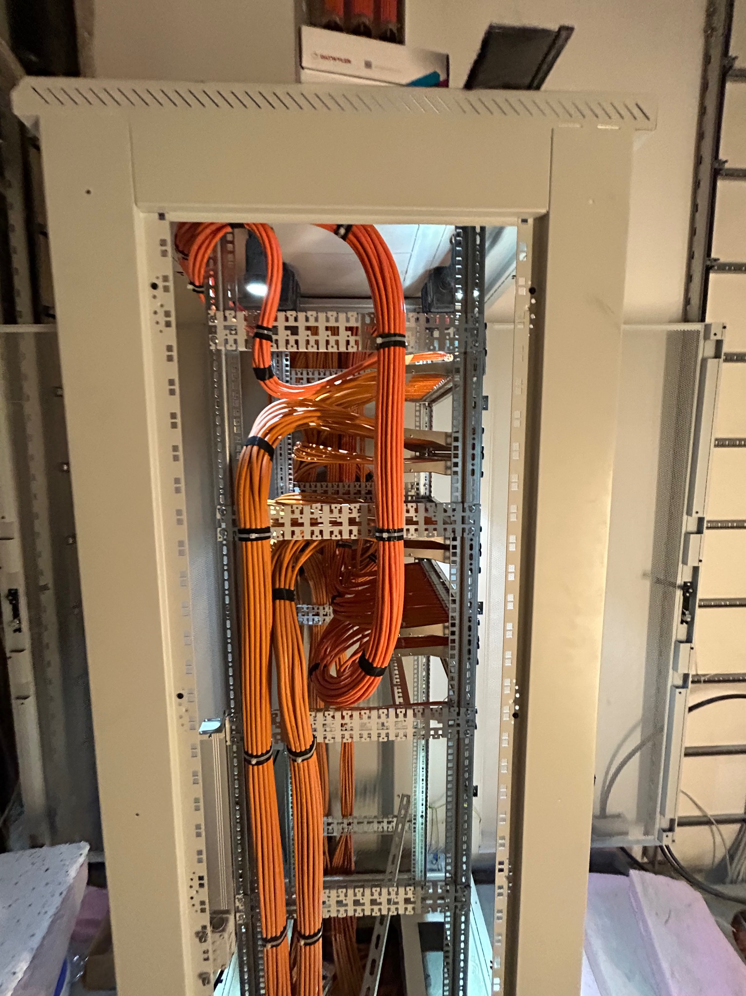 Pomarańczowe kable prowadzone wewnątrz szafy rack, zabezpieczone czarnymi opaskami zaciskowymi, widoczne elementy montażowe szafy.
