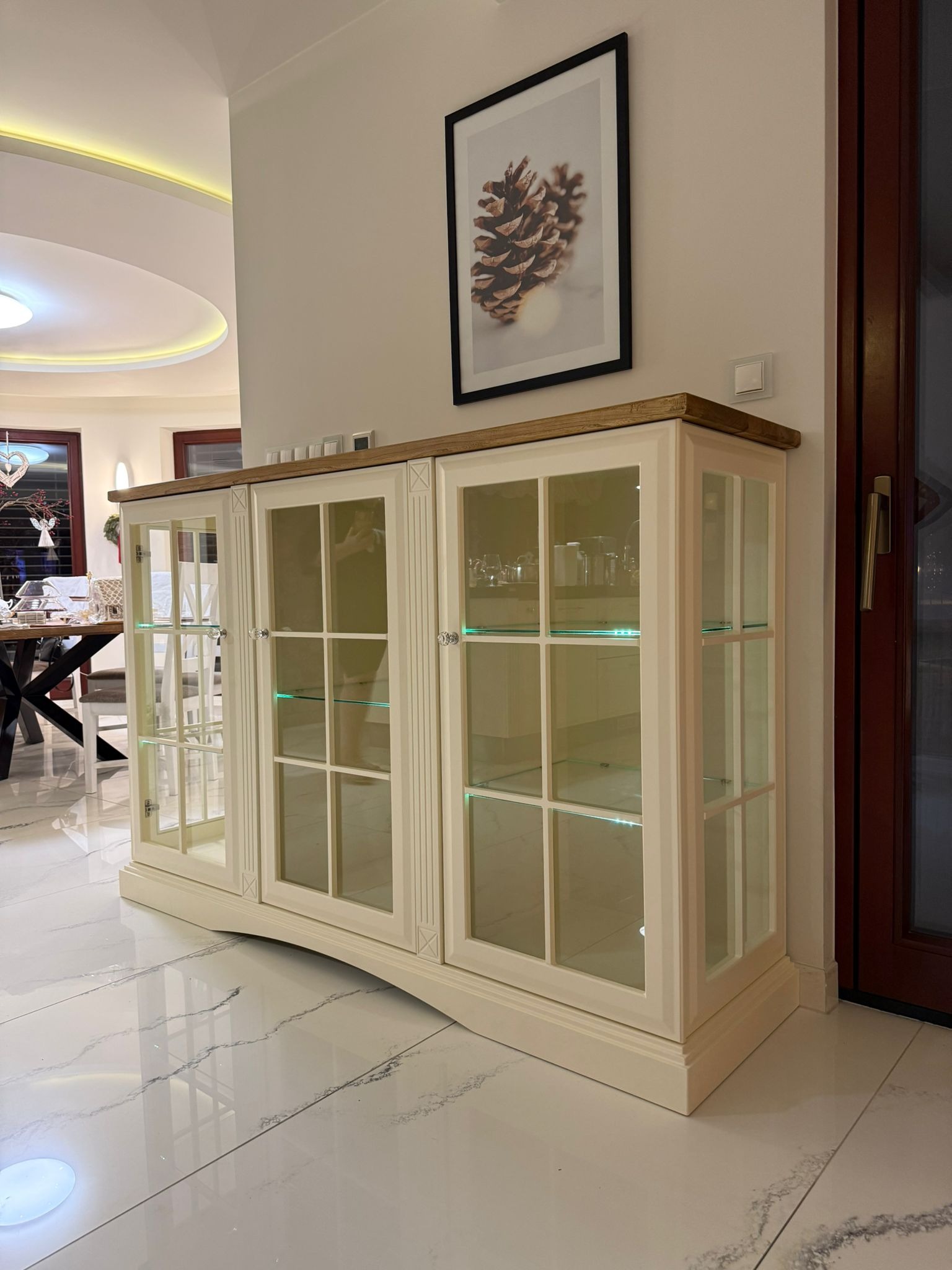 Elegancka, przeszklona witryna w odcieniach bieli i drewna, z delikatnym podświetleniem LED, ustawiona na błyszczącej, marmurowej podłodze w jasnym wnętrzu.