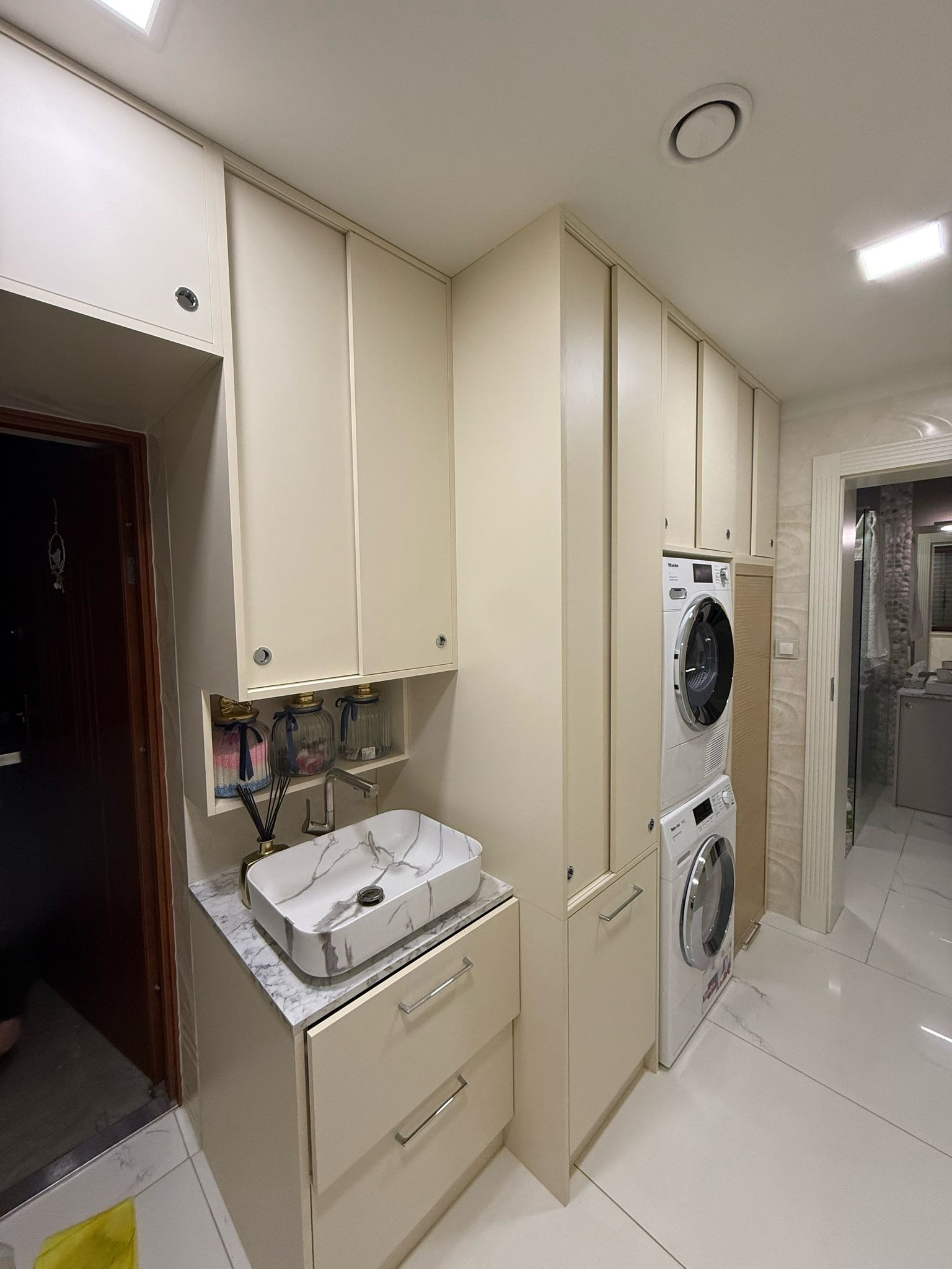 Jasna łazienka z zabudową meblową na wymiar, marmurową umywalką i pralko-suszarką Miele. Minimalistyczny design, funkcjonalne rozwiązanie do małej przestrzeni.