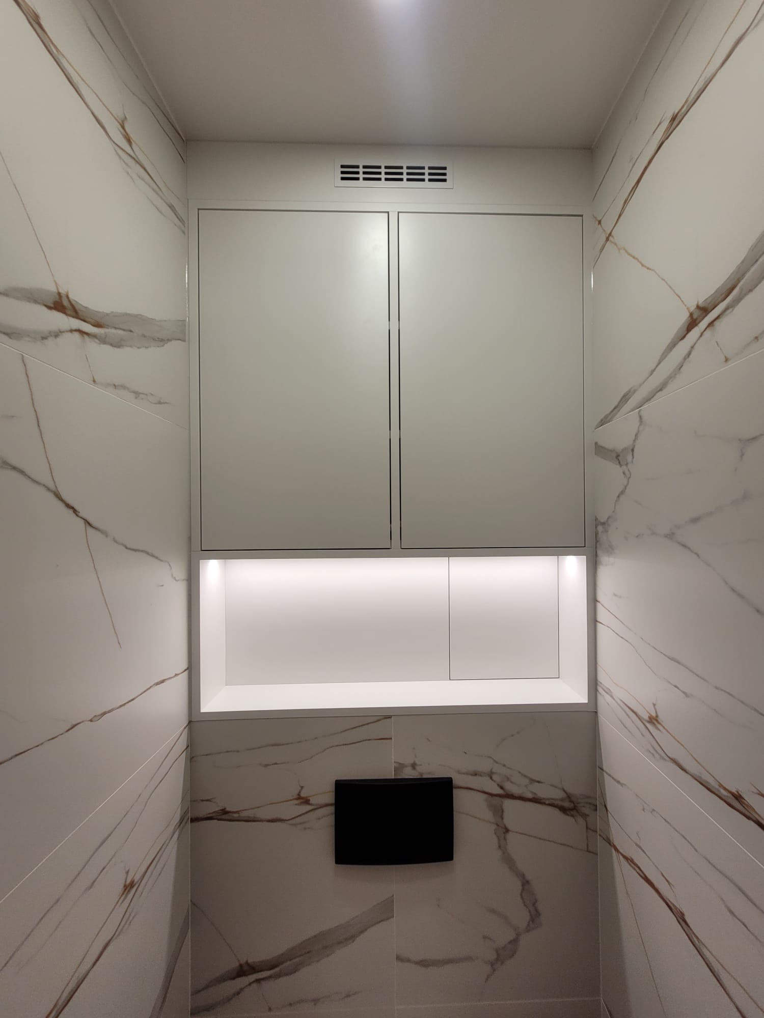 Biała szafka wnękowa z oświetleniem LED, w łazience wykończonej marmurowymi płytkami w Katowicach. Minimalistyczny design, ukryty dostęp do instalacji.