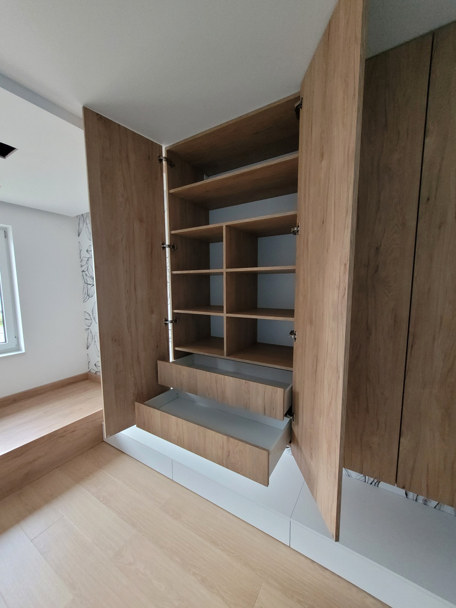 Drewniana szafa z półkami i wysuwanymi szufladami, widok z otwartymi drzwiami ukazujący wnętrze, jasne drewno z widocznym usłojeniem, nowoczesny design.