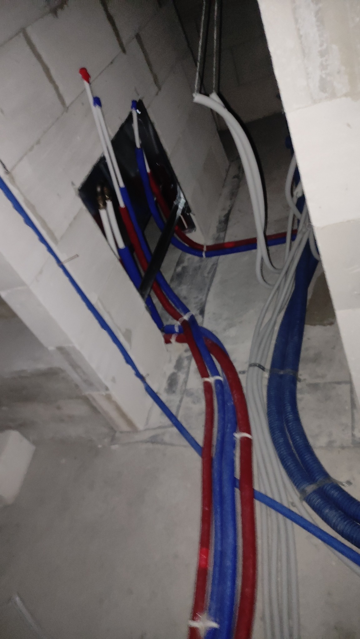 Wiązka rur instalacyjnych w kolorach czerwonym, niebieskim i białym, wychodzących ze ściany z betonu komórkowego, zabezpieczonych opaskami zaciskowymi.