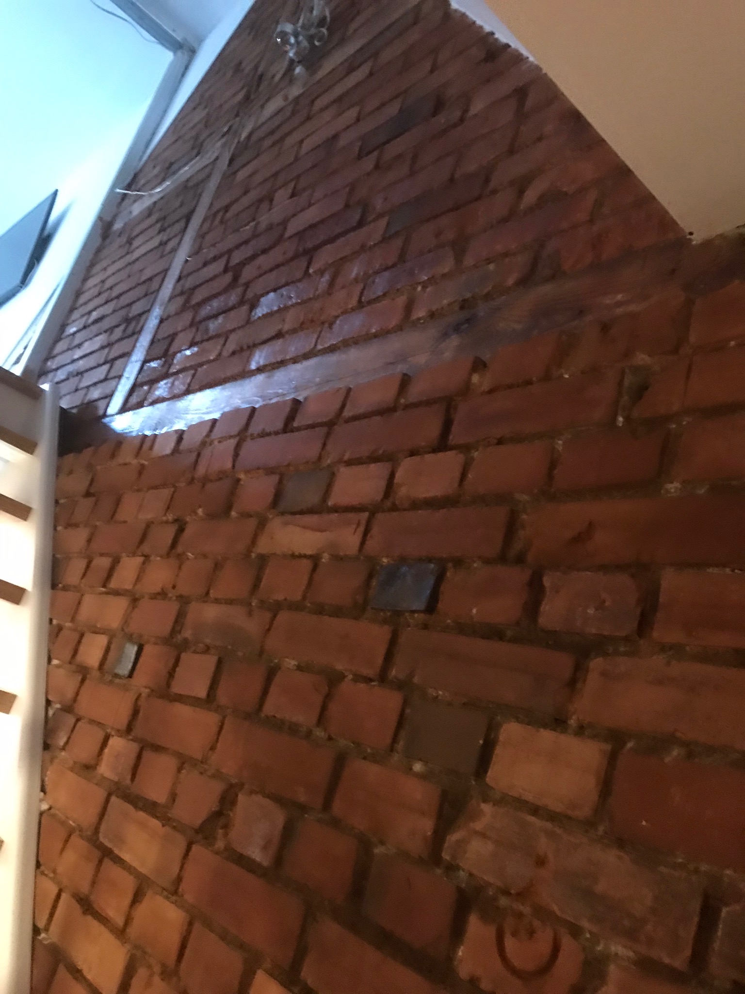 Fragment ściany z czerwonej cegły z widocznym metalowym profilem, surowy wystrój wnętrza w trakcie wykańczania.