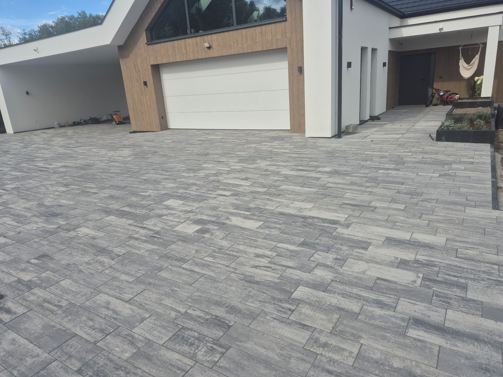 Ułożona szara kostka brukowa na podjeździe do nowoczesnego domu w Wielgolas. Widoczne garaż i wejście do budynku. Charakterystyczny wzór kostki.