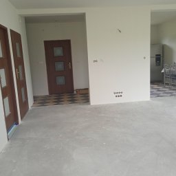 Mariusz Godzina - Wnętrze domu po wylewce, ściany przygotowane do malowania, widoczne gniazdka elektryczne i drzwi wewnętrzne z szybkami.