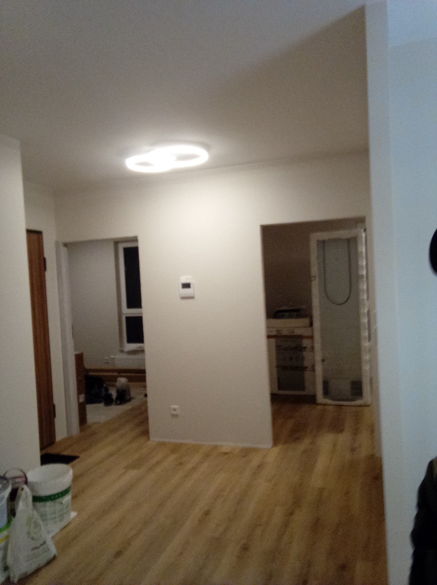 Wnętrze po remoncie: Jasne ściany, drewnopodobna podłoga, widoczne puszki z farbą w rogu, drzwi do dwóch pomieszczeń w tle.