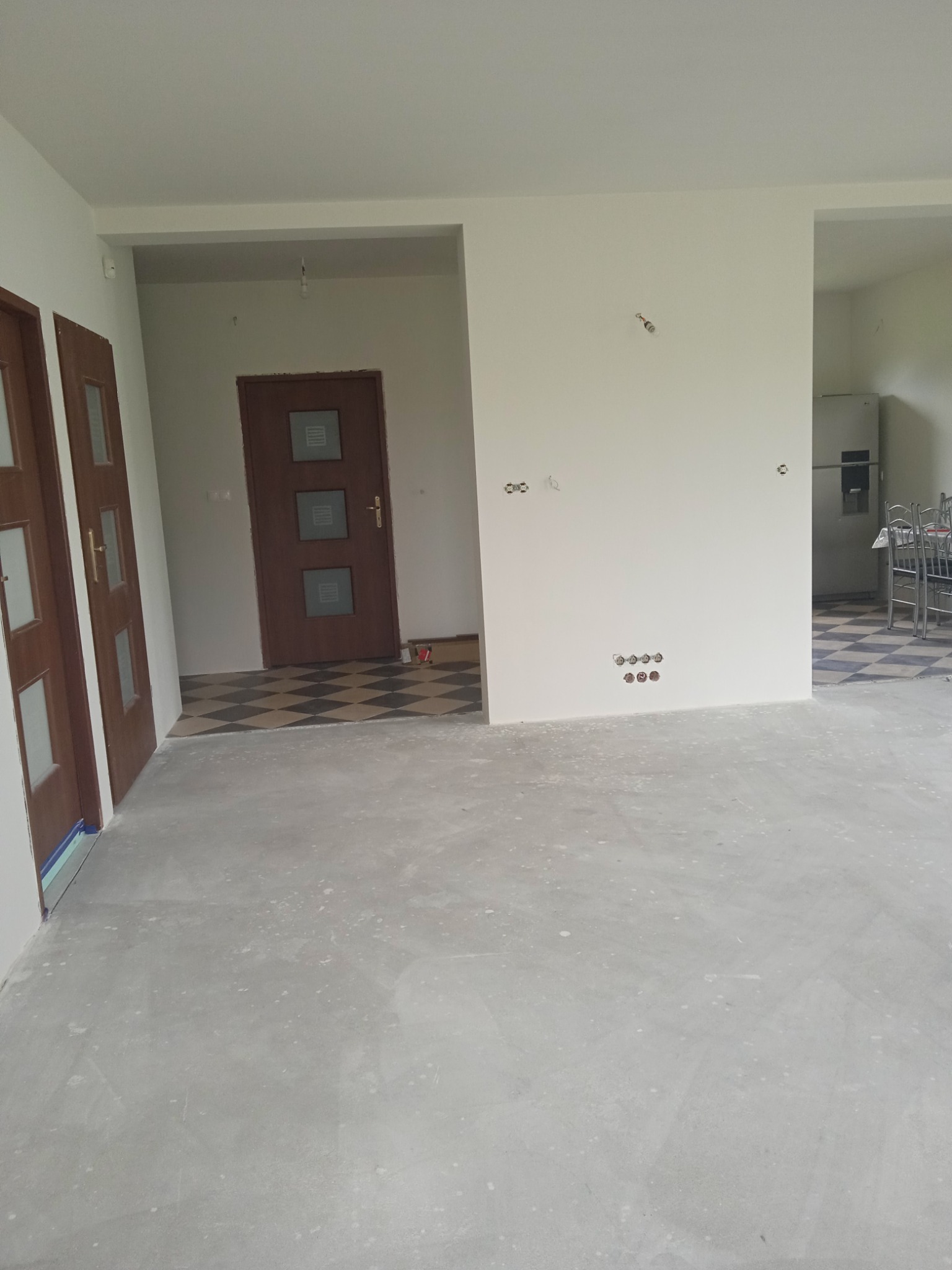 Wnętrze domu po wylewce, ściany przygotowane do malowania, widoczne gniazdka elektryczne i drzwi wewnętrzne z szybkami.