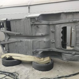 Hydro-piaskowanie Mateusz Czaplicki - Podwozie samochodu po obróbce, przygotowane do dalszych prac, wsparte na oponach i piankowych podkładkach, widoczne przewody na piaszczystym podłożu.