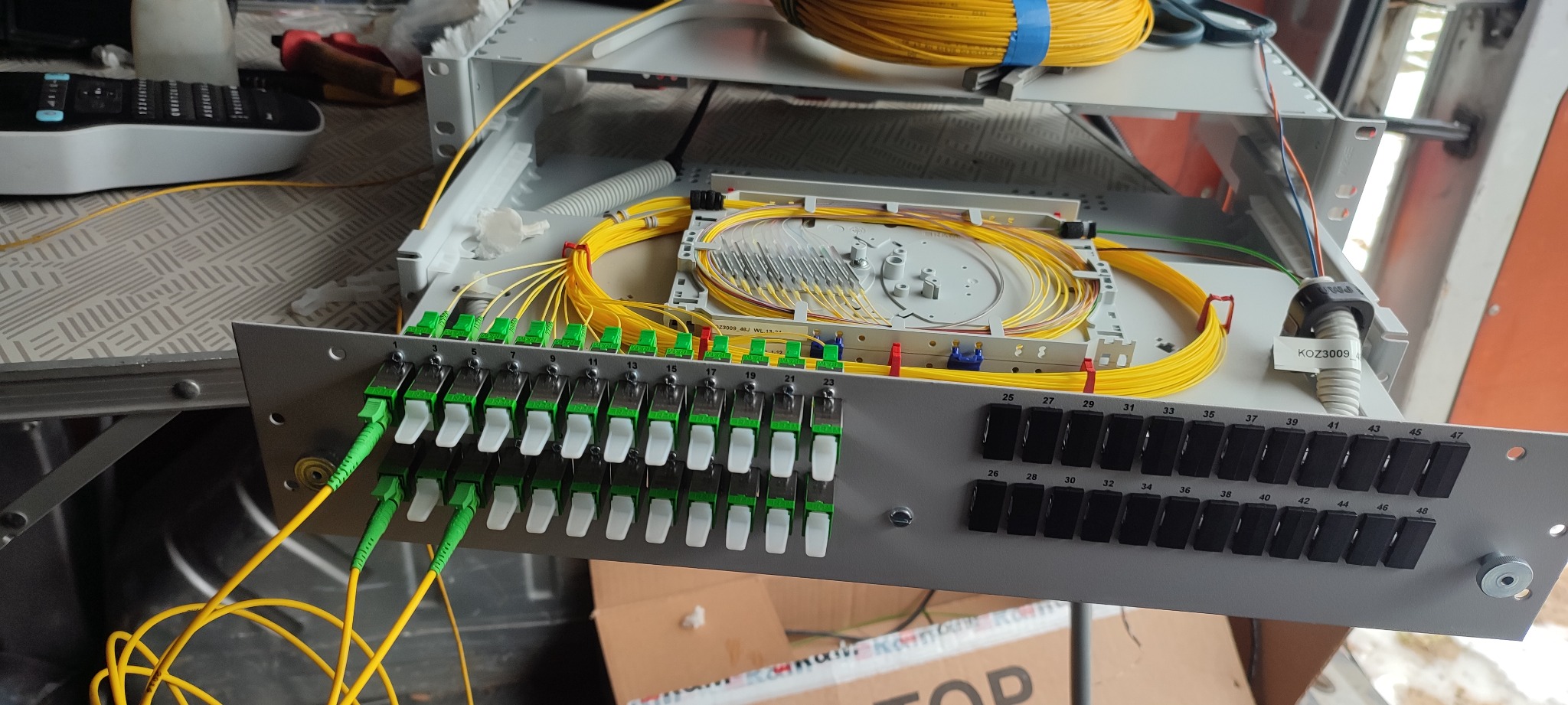 Panel krosowy światłowodowy z podłączonymi kablami światłowodowymi, widoczne złącza SC/APC z zielonymi wtykami, żółte kable ułożone wewnątrz kasety światłowodowej.