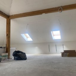 Mdkremonty - Poddasze w trakcie prac wykończeniowych: gładzie, drewniane belki stropowe, okna dachowe, grzejniki, worki i puszki z farbami. Widok ogólny, surowy stan.