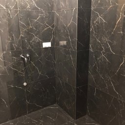 Mdkremonty - Kabina prysznicowa wyłożona czarnymi płytkami imitującymi marmur z białymi żyłami, widoczna armatura prysznicowa.