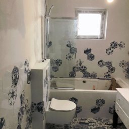 Mdkremonty - Łazienka w trakcie wykańczania z białą armaturą, heksagonalnymi płytkami z niebieskim wzorem na ścianach i podłodze, widoczna wanna z zamontowaną kabiną prysznicową.