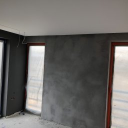 Mdkremonty - Pokój w trakcie szpachlowania ścian na szaro, okna zabezpieczone folią, widoczne kable wystające z sufitu.