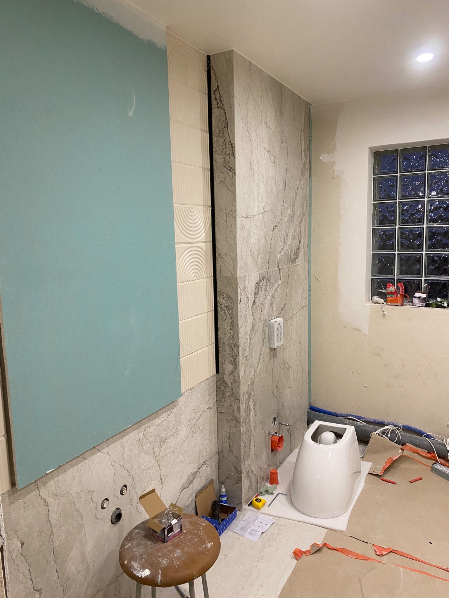 Remont łazienki w Warszawie: Montaż płyty karton-gips, układanie płytek imitujących marmur i instalacja podwieszanej toalety. Widoczne narzędzia i materiały budowlane.