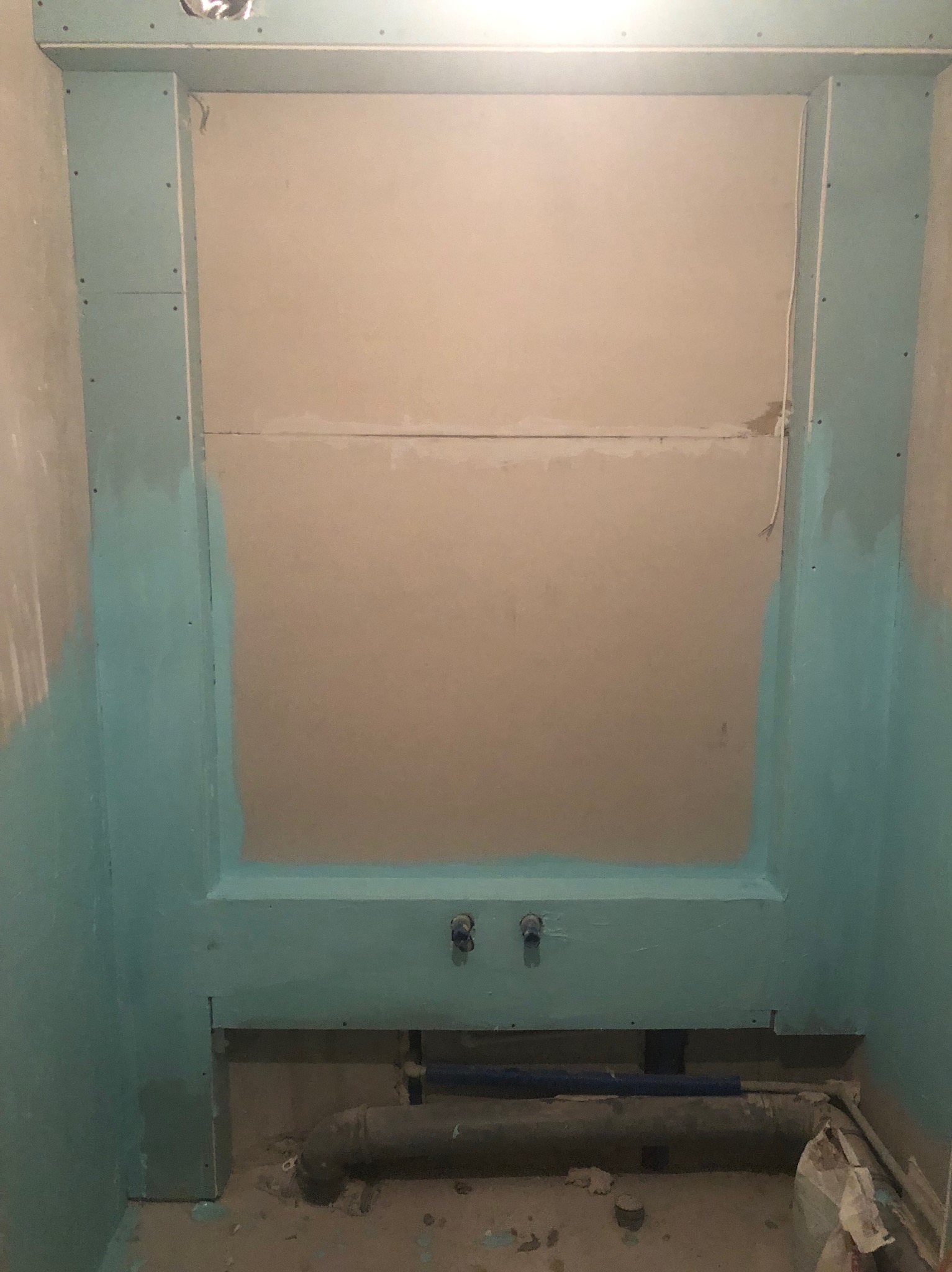 Montaż płyt gipsowo-kartonowych w łazience, widoczne rury i instalacja wodna przed zabudową. Częściowo pomalowane na niebiesko.