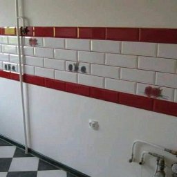 nie podano - Ściana wyłożona białymi i czerwonymi płytkami ceramicznymi z motywem owoców, widoczny fragment podłogi w szachownicę, instalacja wodna i rura pionowa.