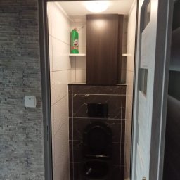 nie podano - Nowoczesna łazienka z czarną miską WC, wykończona płytkami w różnych wzorach i kolorach, widoczna przez otwarte białe drzwi.