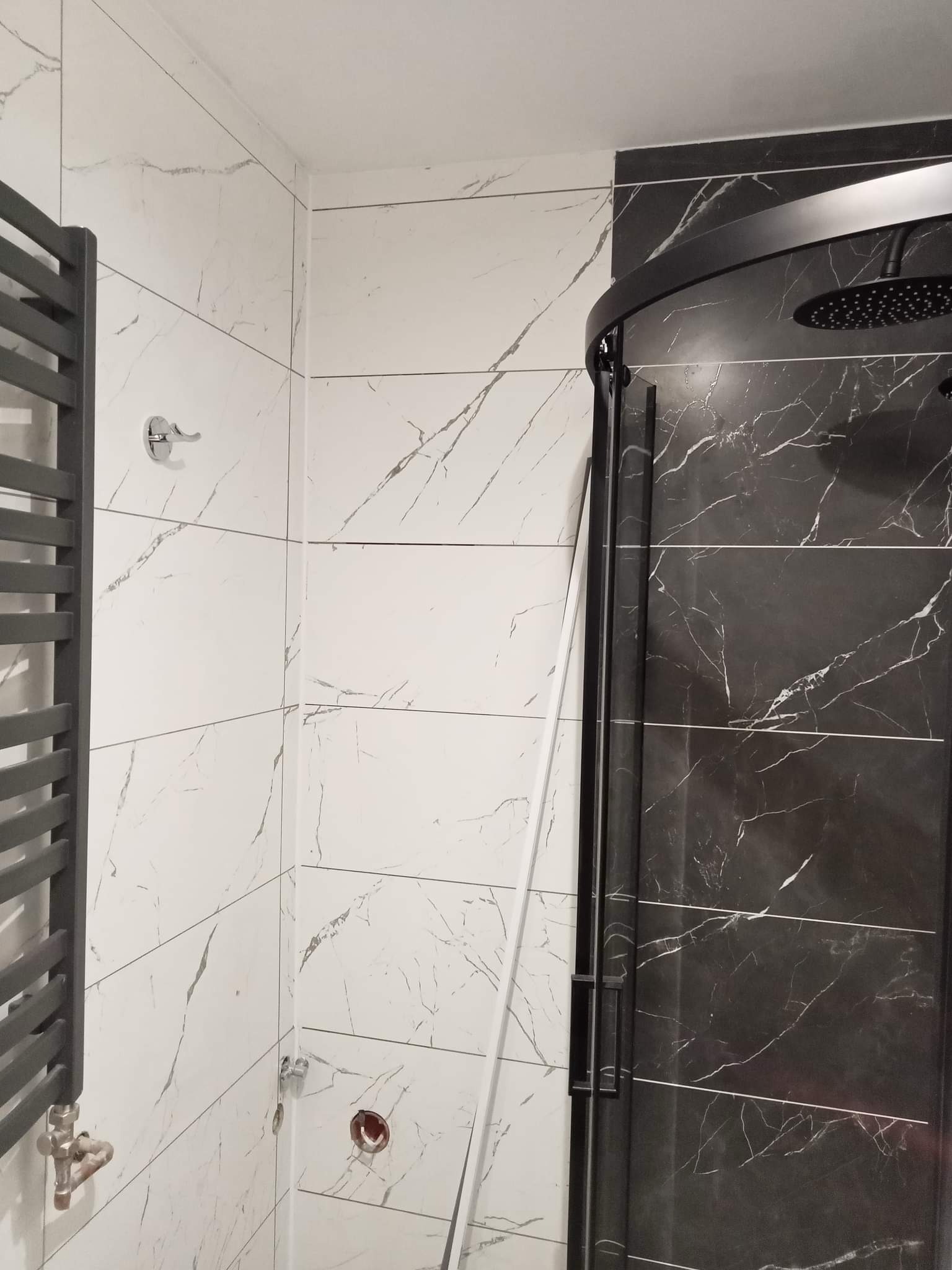 Nowoczesna łazienka z czarno-białymi płytkami imitującymi marmur, czarną kabiną prysznicową typu walk-in i szarym grzejnikiem drabinkowym.