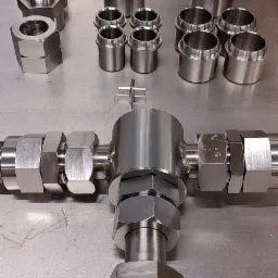 Precyzyjnie wykonane, metalowe elementy z gwintami, złączki i nakrętki o heksagonalnym kształcie, ułożone na metalowym stole roboczym z perforowaną ścianką w tle.